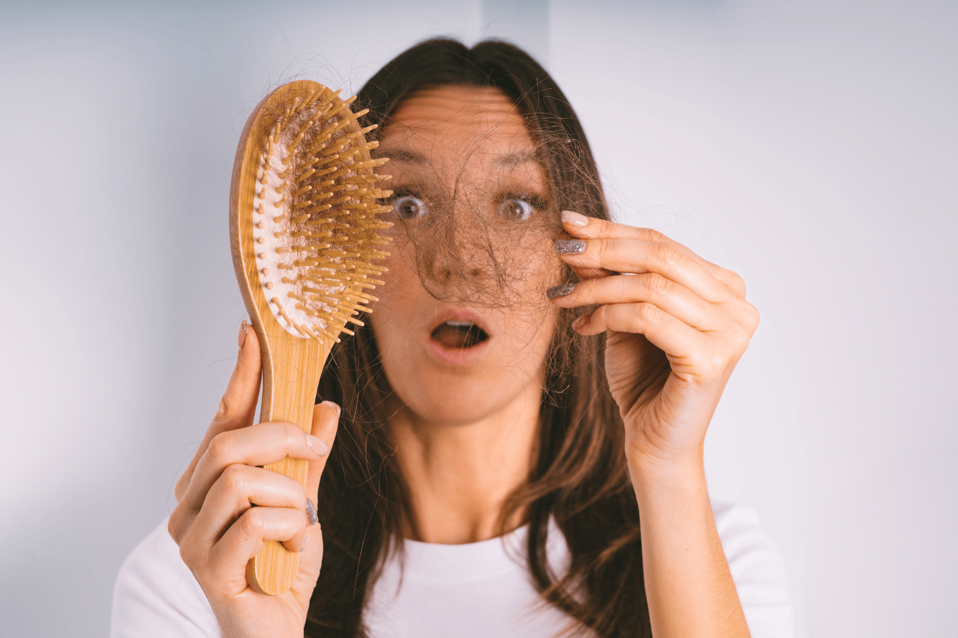 Woman looking surprised while holding a hairbrush and a clump of shed hair.