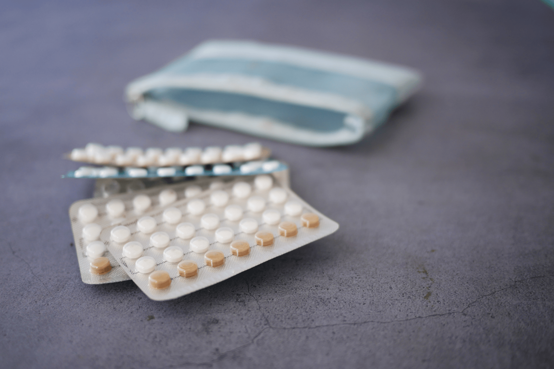 Close-up of blister packs of birth control pills on a table with a small pouch in the background.