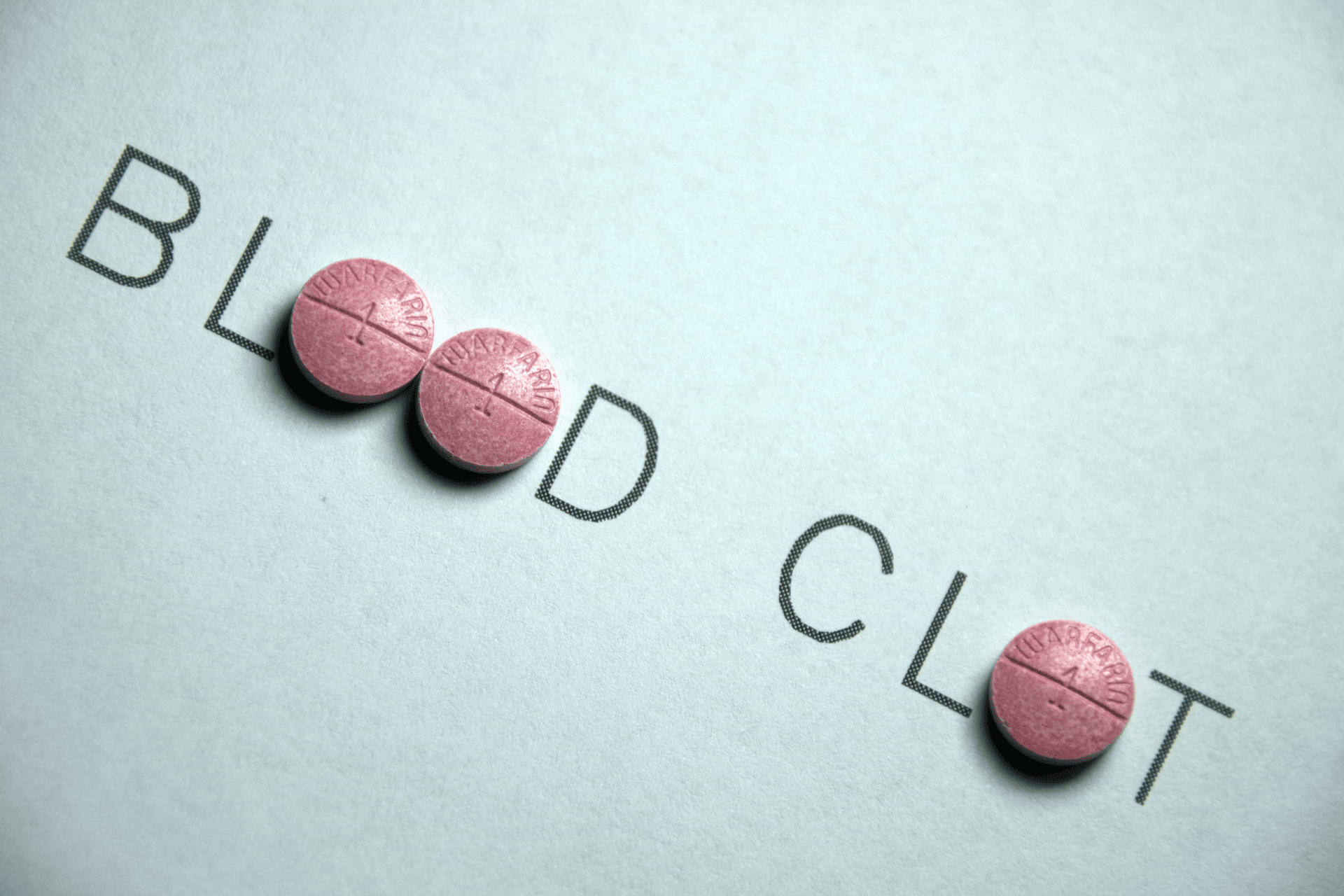 Pink pills placed over the words “BLOOD CLOT,” suggesting blood clot medication or treatment.