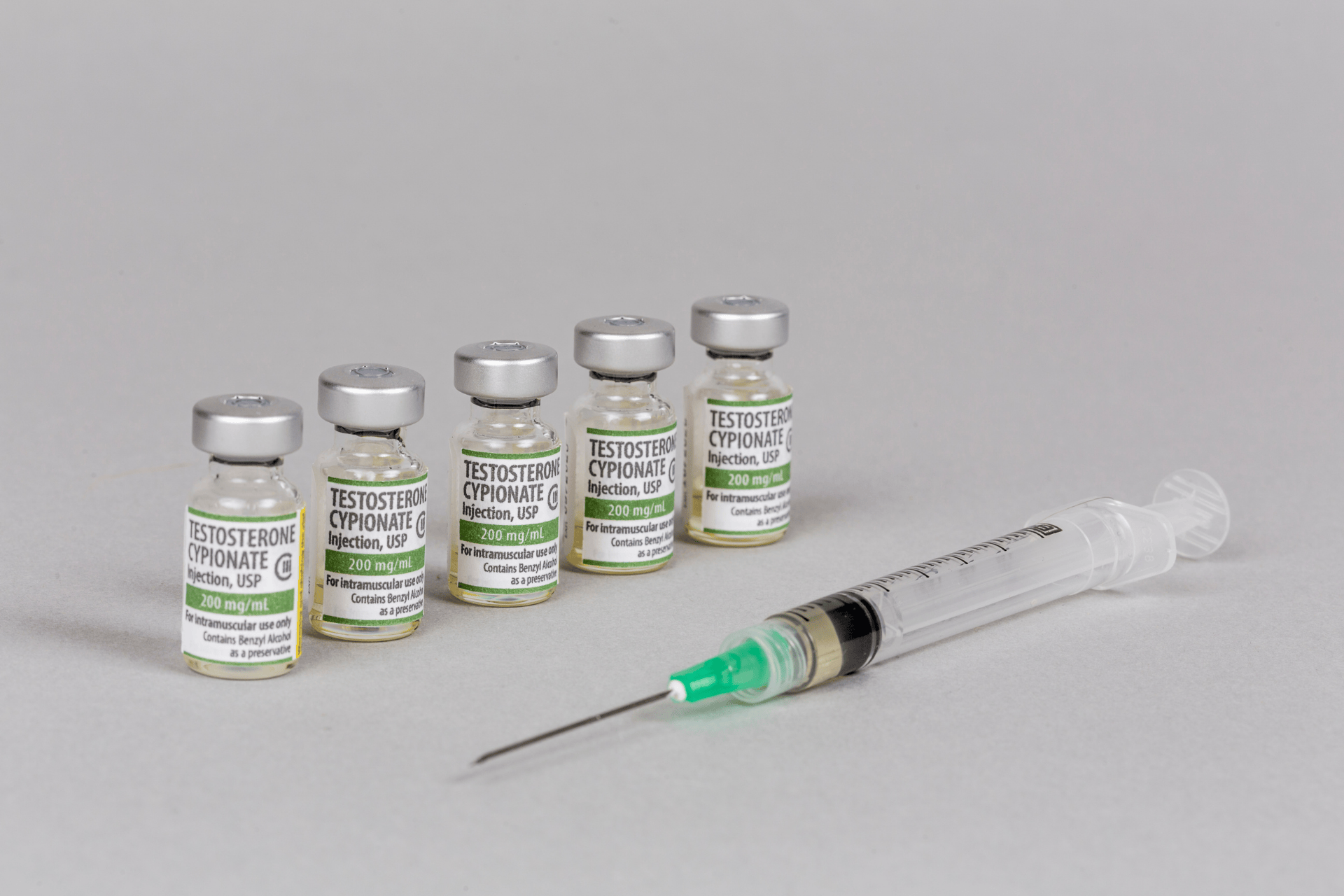 Vials of testosterone cypionate injection with a syringe on a gray surface.