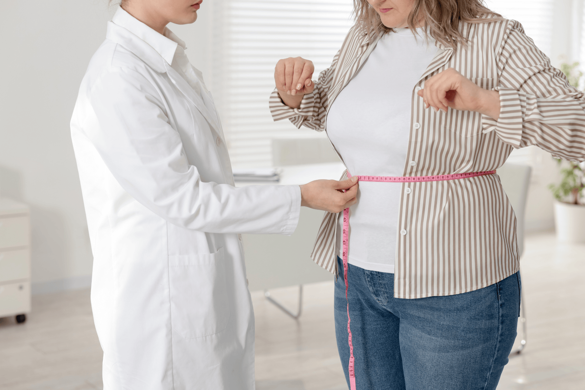 Healthcare professional measuring a patient’s waist with a pink measuring tape.