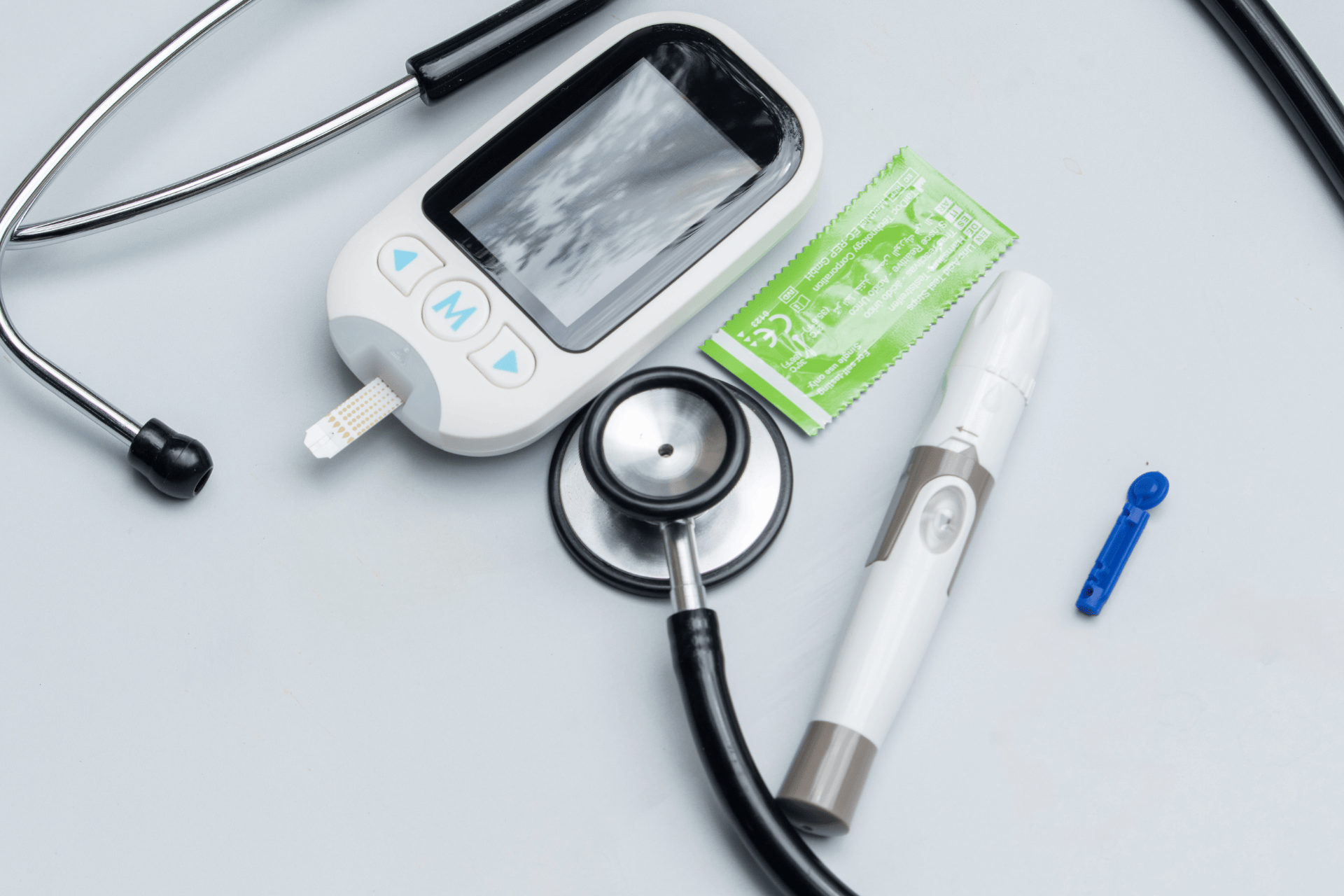 Diabetes testing kit and stethoscope on a white surface.