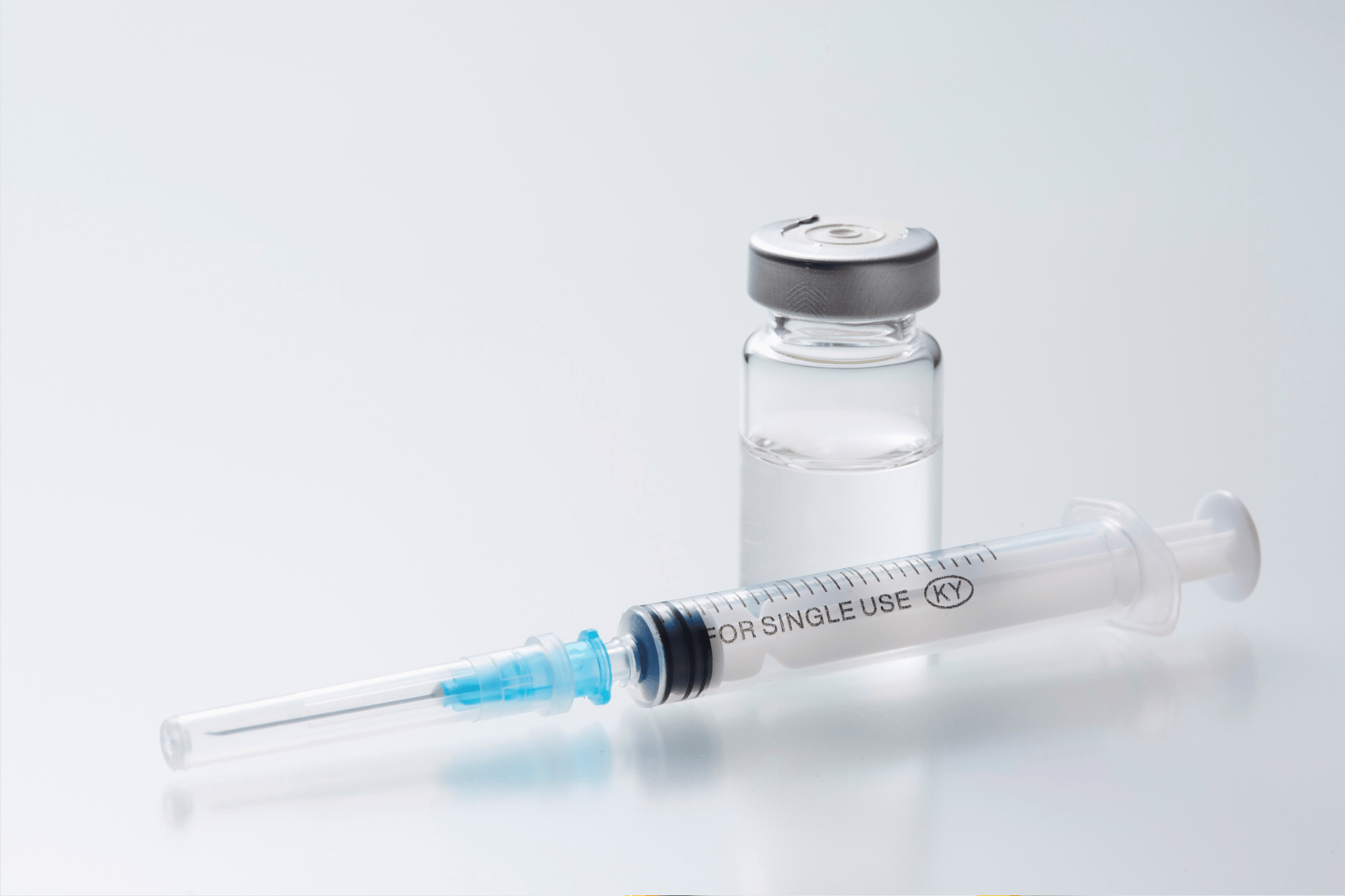 Close-up of a syringe and a vial of clear liquid on a white background.