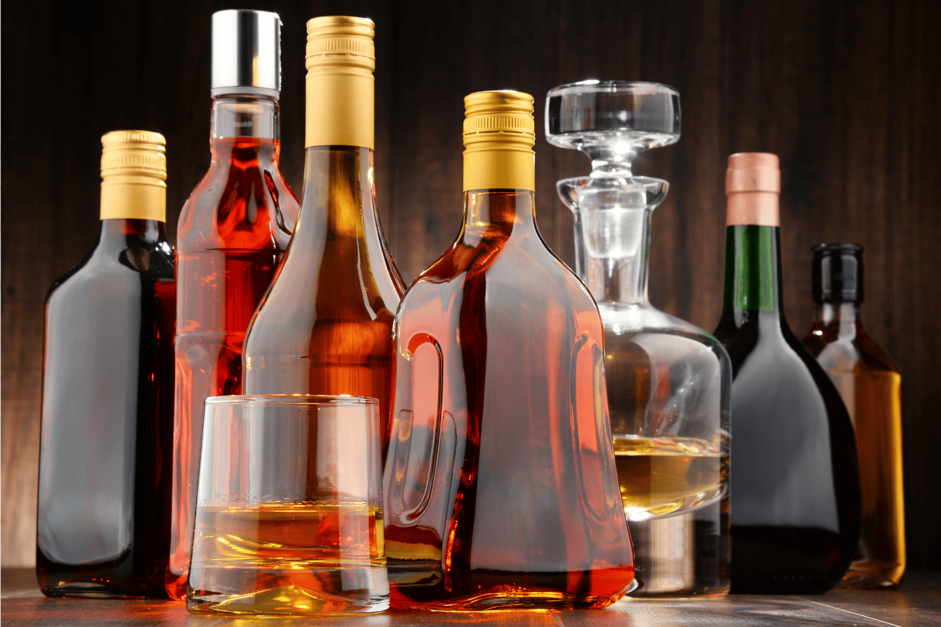 Assorted liquor bottles and a glass of whiskey on a wooden surface.