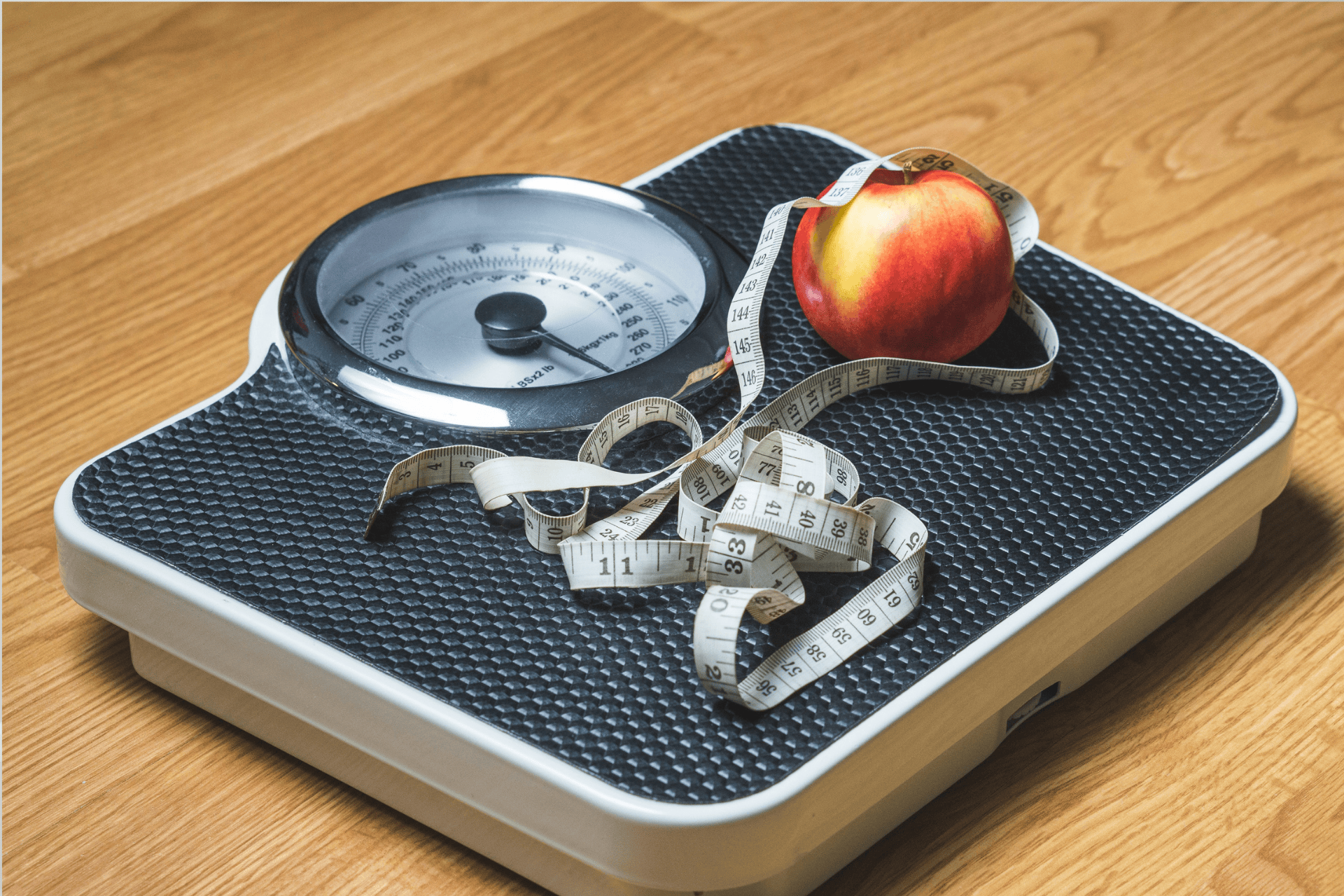 Bathroom scale with a measuring tape and an apple on top, symbolizing weight management.