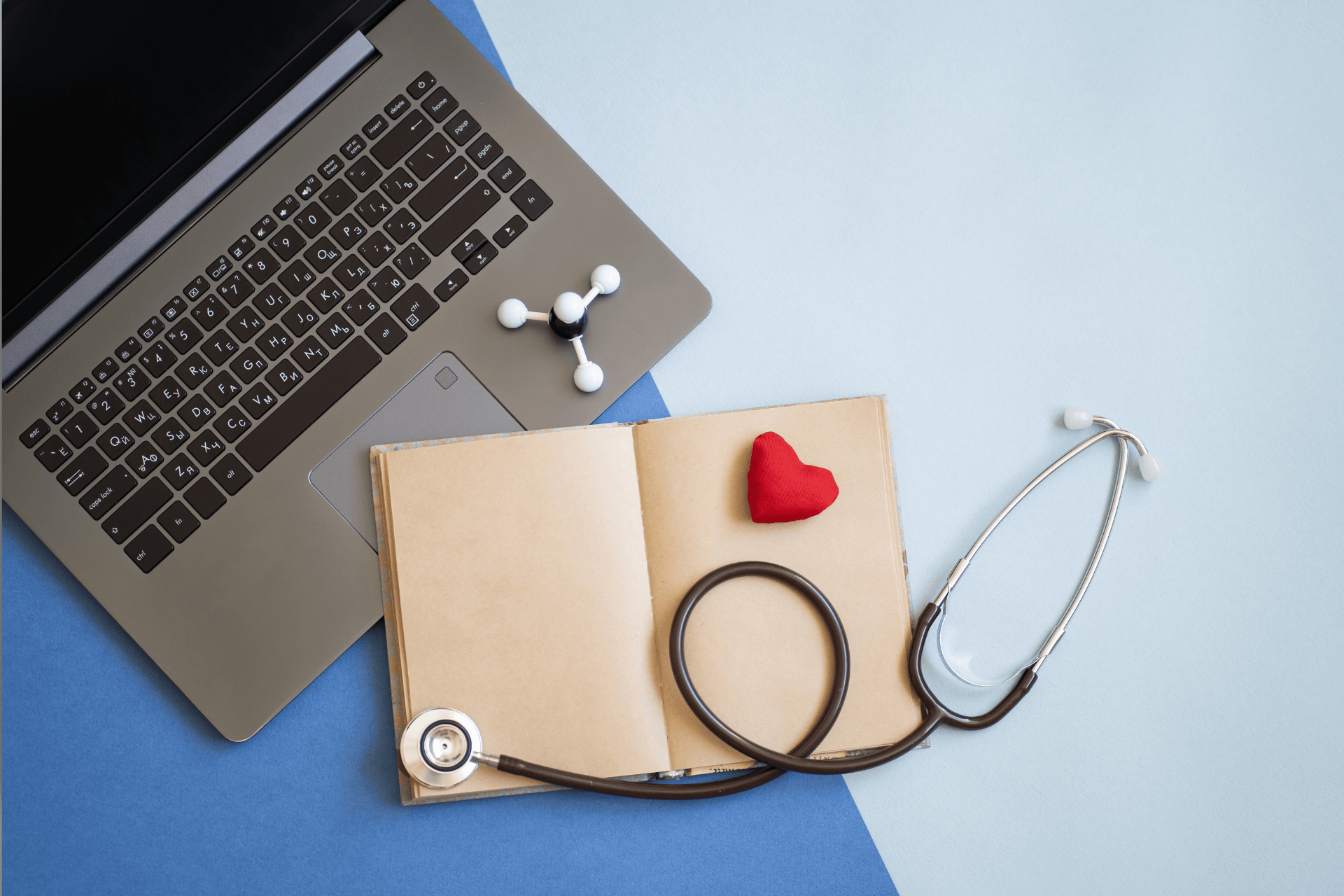 Laptop, stethoscope, and small red heart on an open notebook representing healthcare and technology.