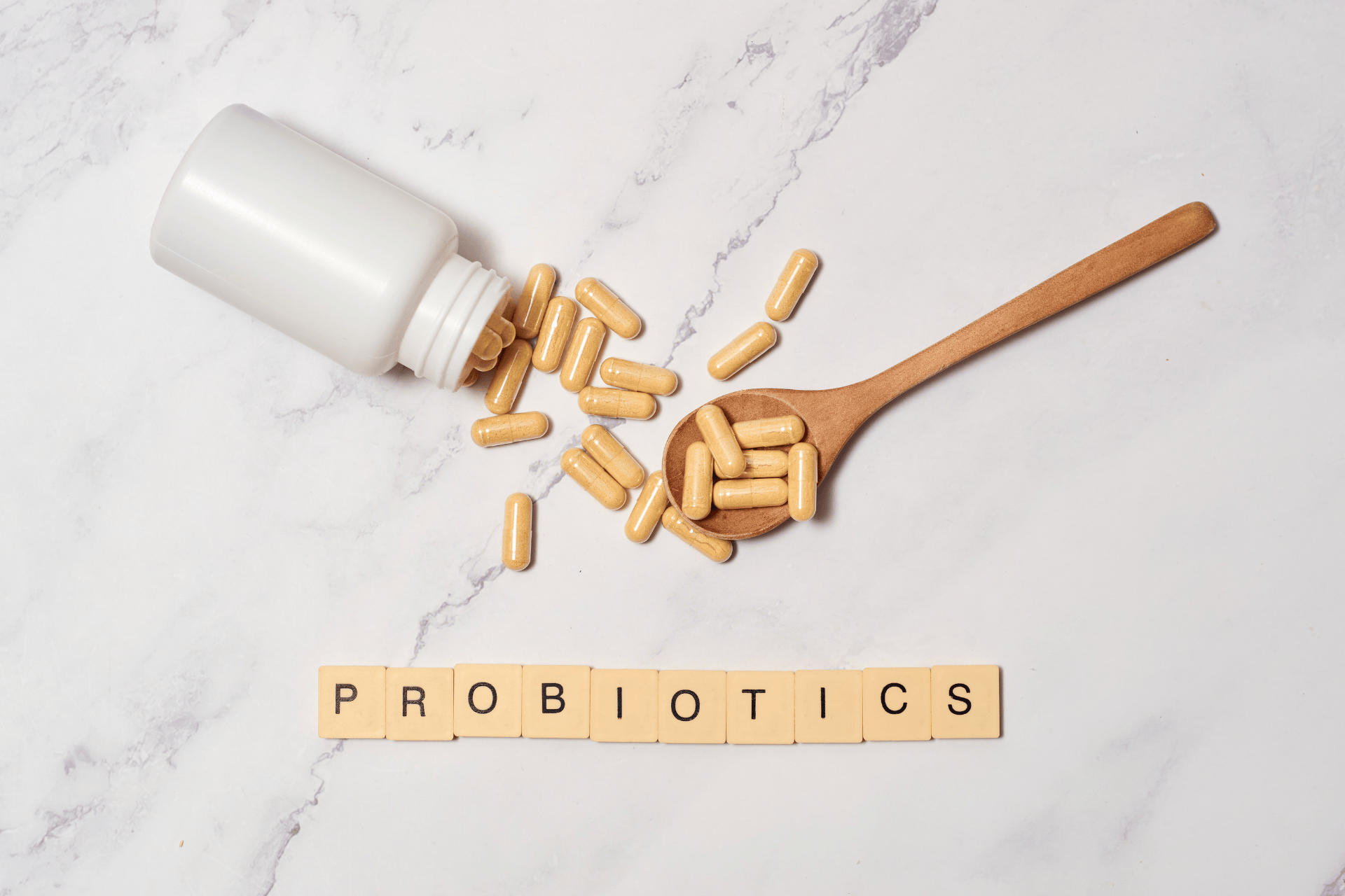 Capsules spilled from a bottle and a wooden spoon with tiles spelling ‘PROBIOTICS’.