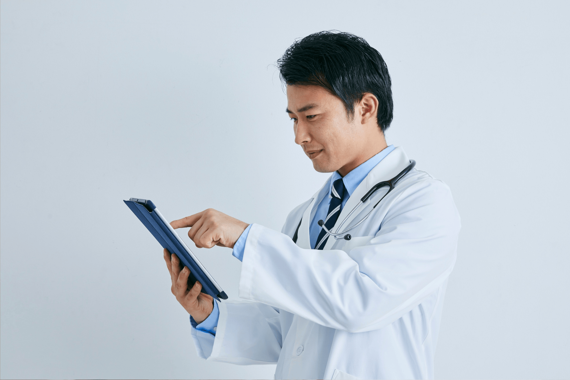 Doctor using a digital tablet while wearing a white coat and a stethoscope.