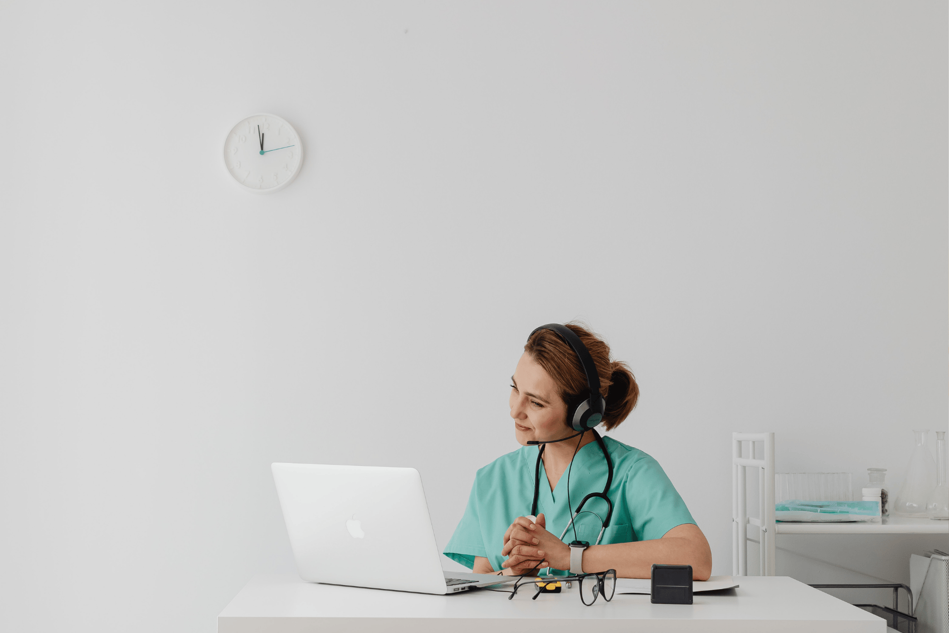 Healthcare professional wearing scrubs and a headset using a laptop for an online consultation.
