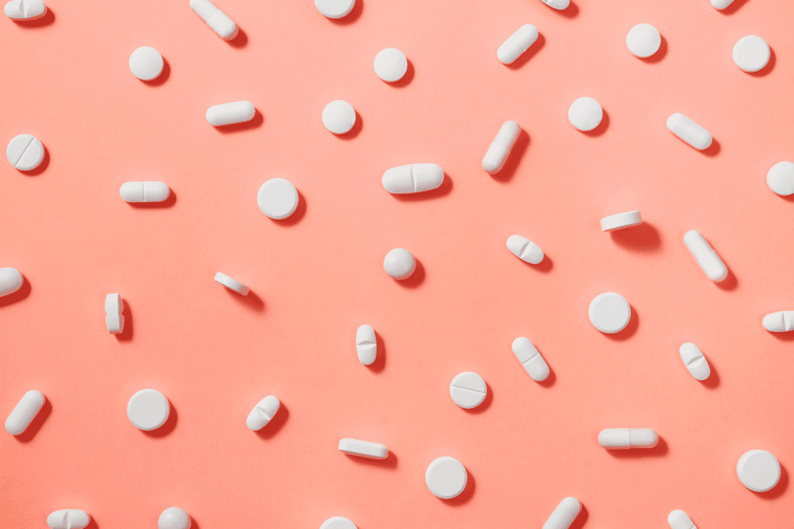White pills scattered across a coral-colored background