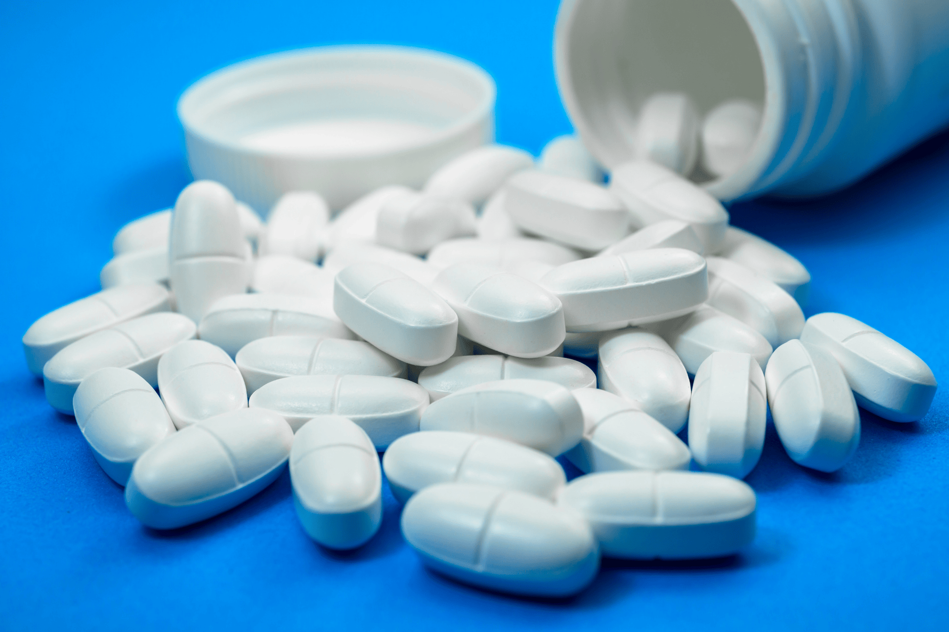 White tablets spilled from an open pill bottle on a blue background