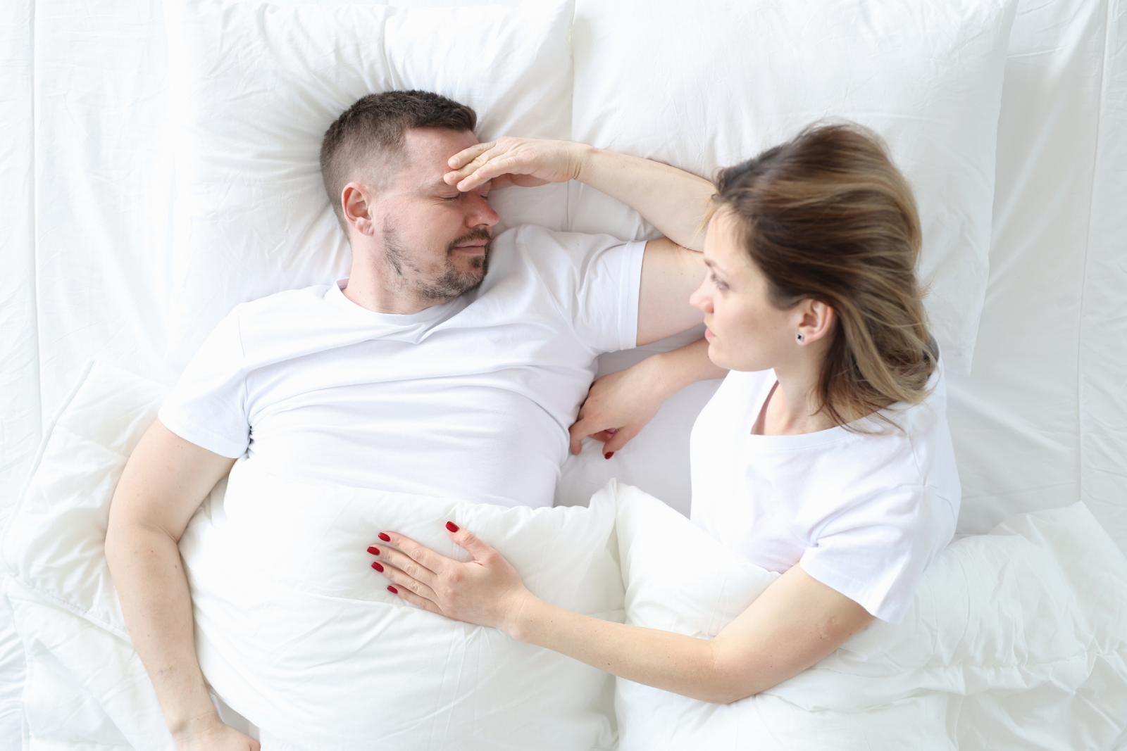 Woman comforting a man lying in bed who appears unwell or distressed.
