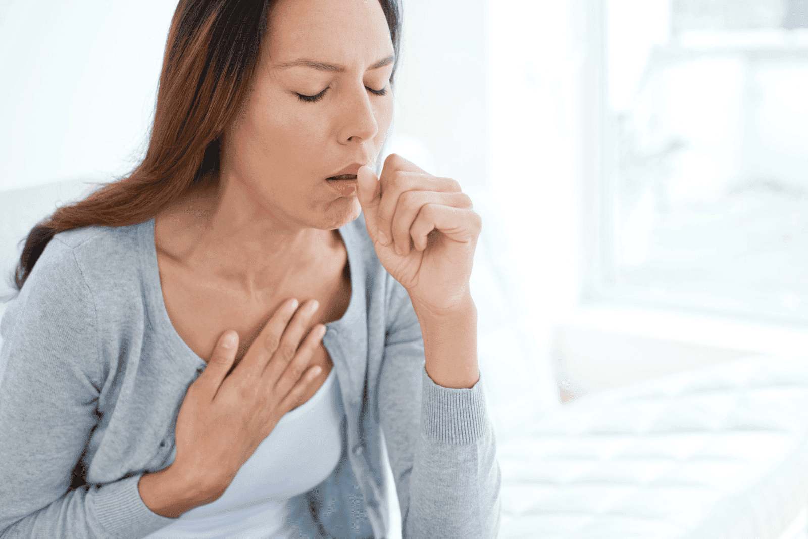 Woman coughing with one hand on her chest, appearing to experience respiratory discomfort.