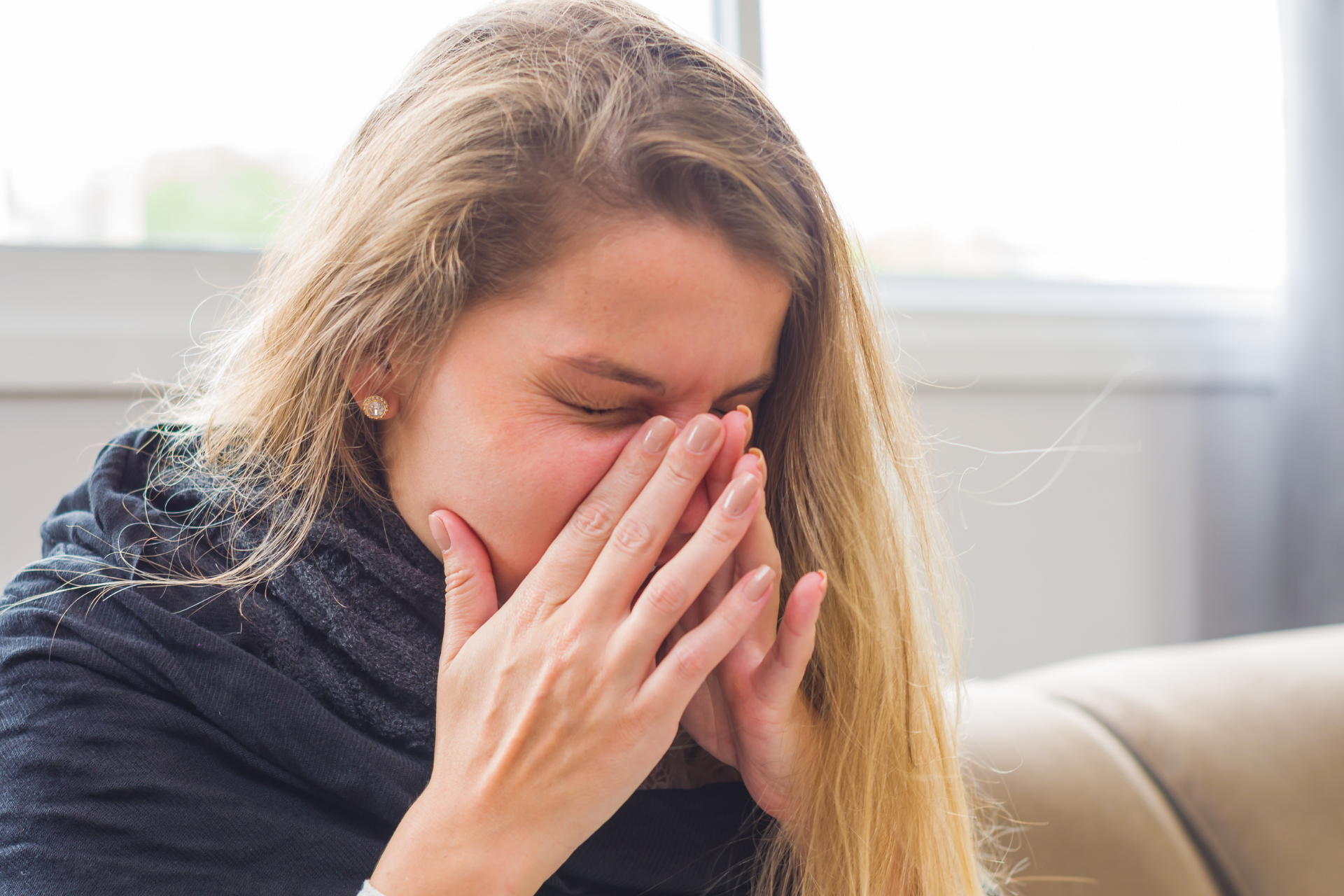 Woman covering her mouth and nose while coughing, appearing uncomfortable or ill indoors