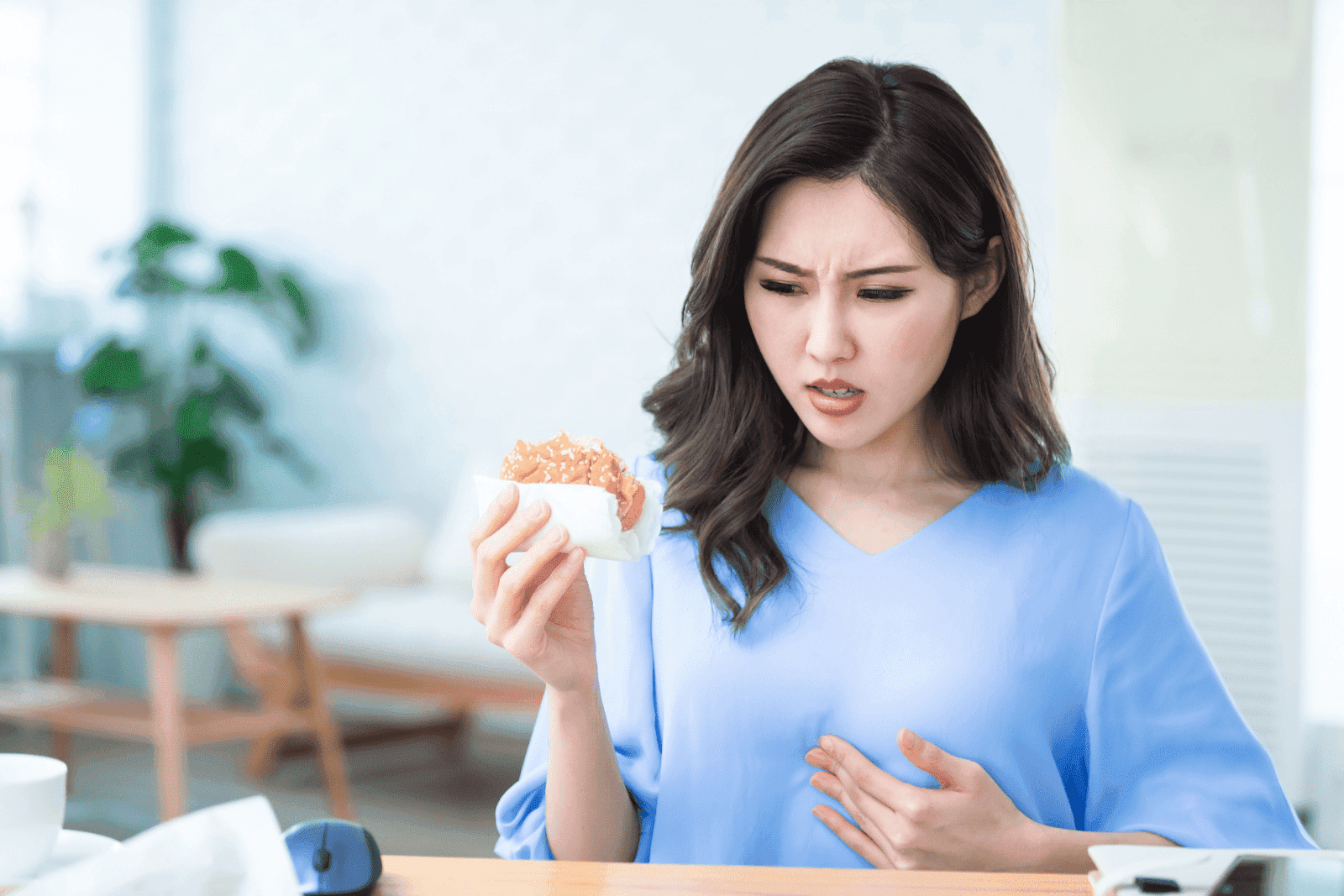 Woman holding a burger and touching her chest with a concerned expression