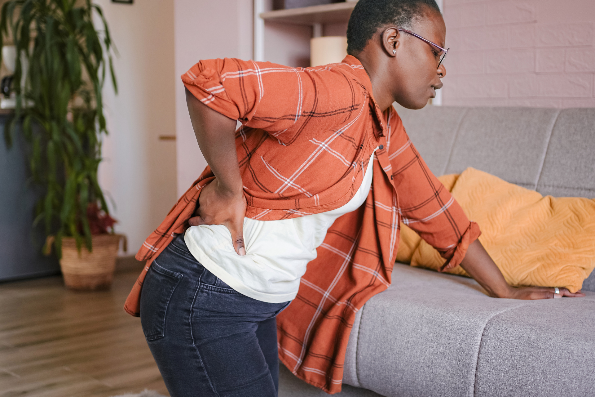 Woman holding her lower back in pain while leaning on a couch at home