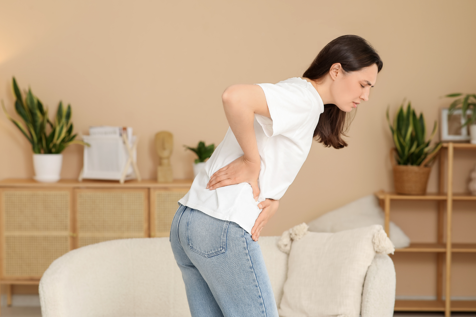 Woman holding her lower back in pain while standing in a living room