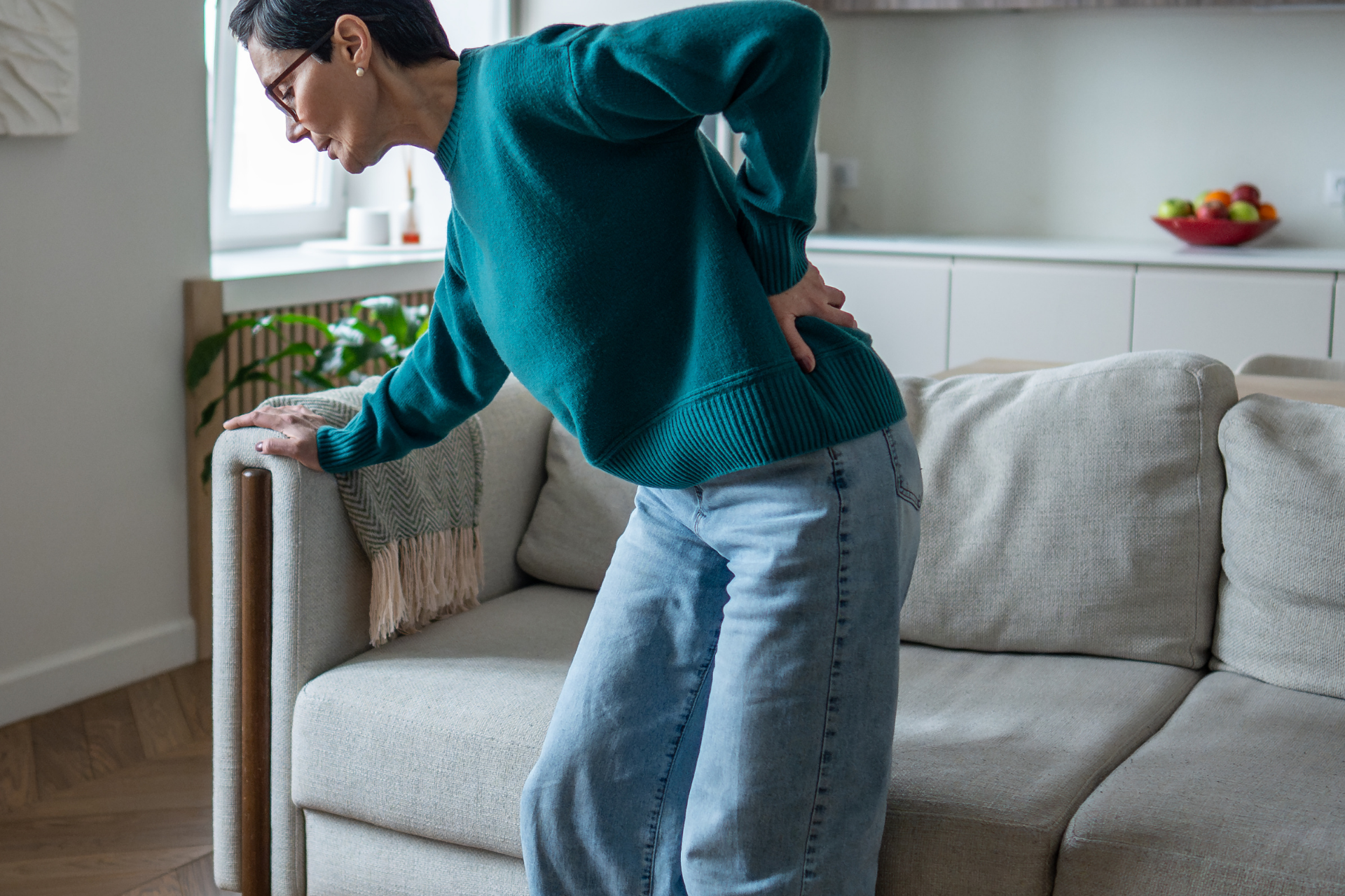 Woman holding her lower back in pain while standing up from a couch