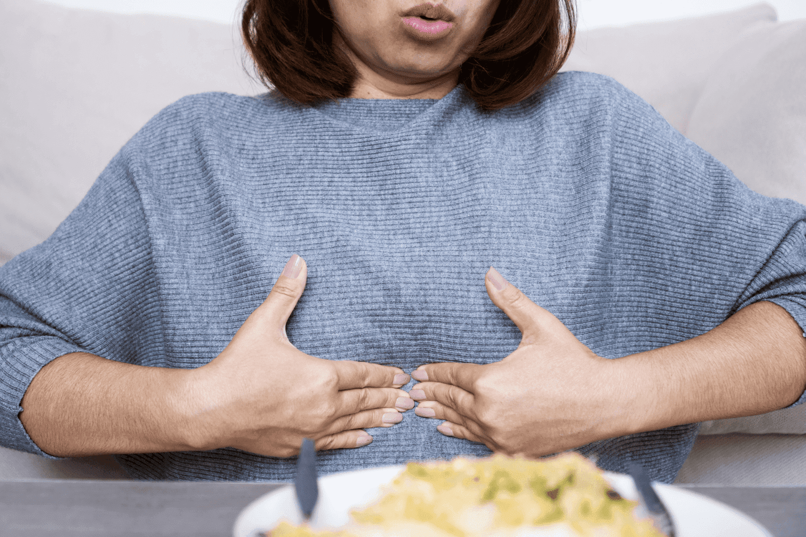 Woman holding her upper abdomen, appearing to experience discomfort after eating