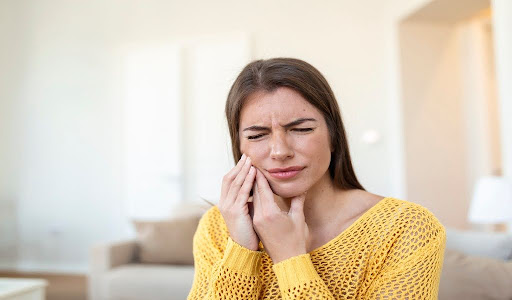 Close-up of a woman grimacing, holding her jaw due to tooth pain.