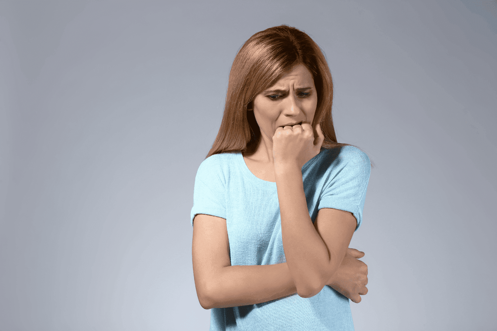 Woman in blue shirt biting her fist, looking anxious.