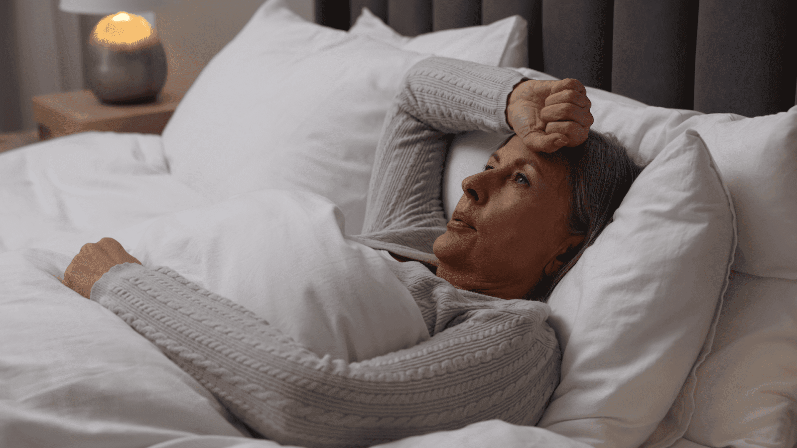 Woman lying in bed, and wiping her forehead from night sweats.