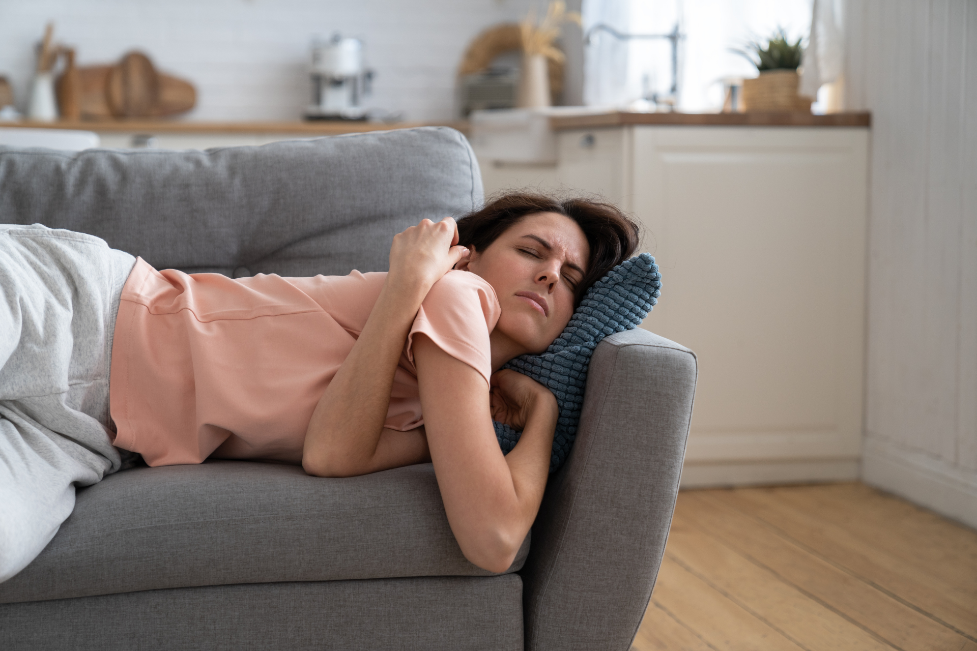 Woman lying on a couch with a pained expression, resting her head on a pillow