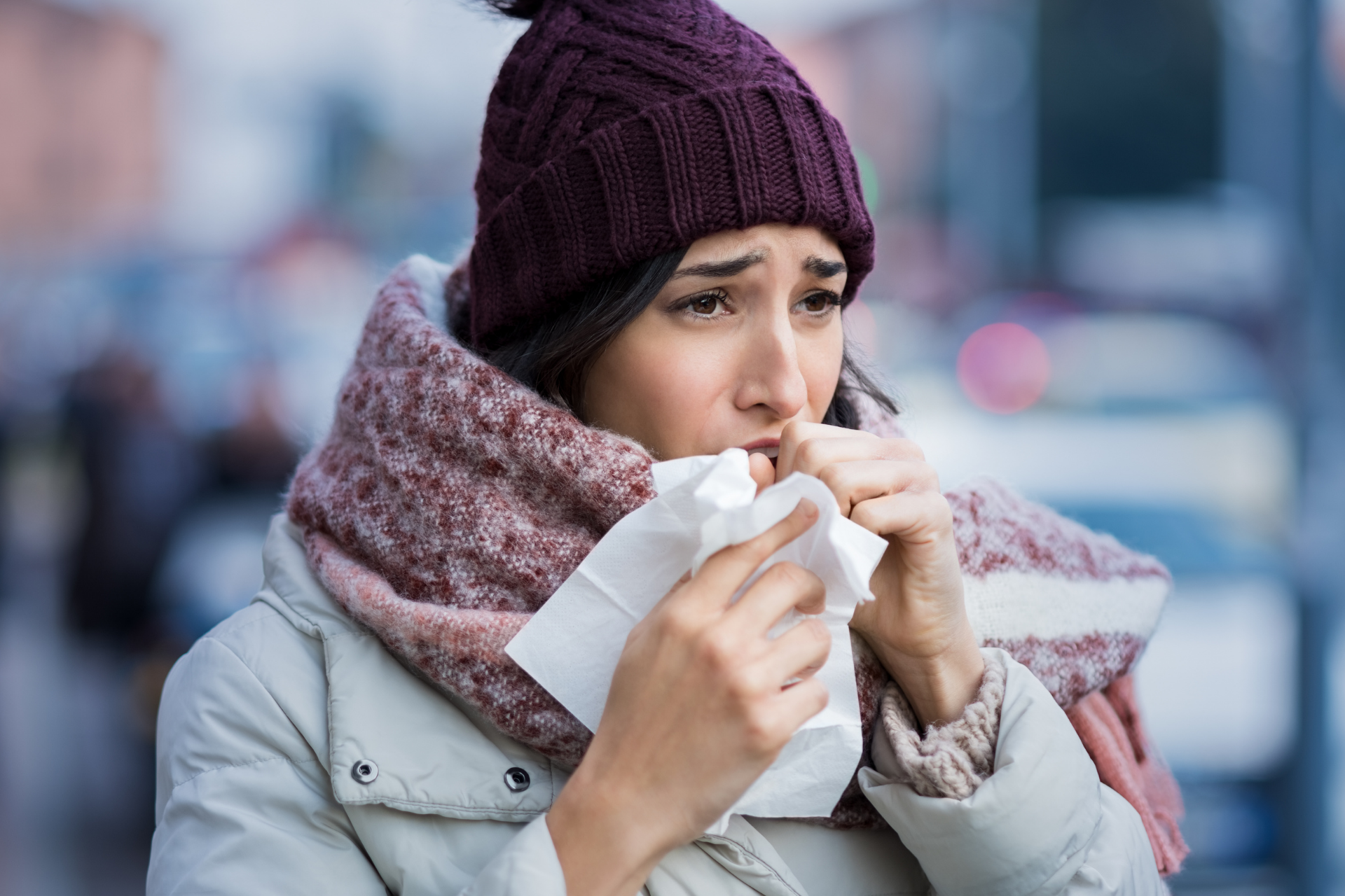 Woman outdoors holding a tissue and appearing ill while dressed for cold weather