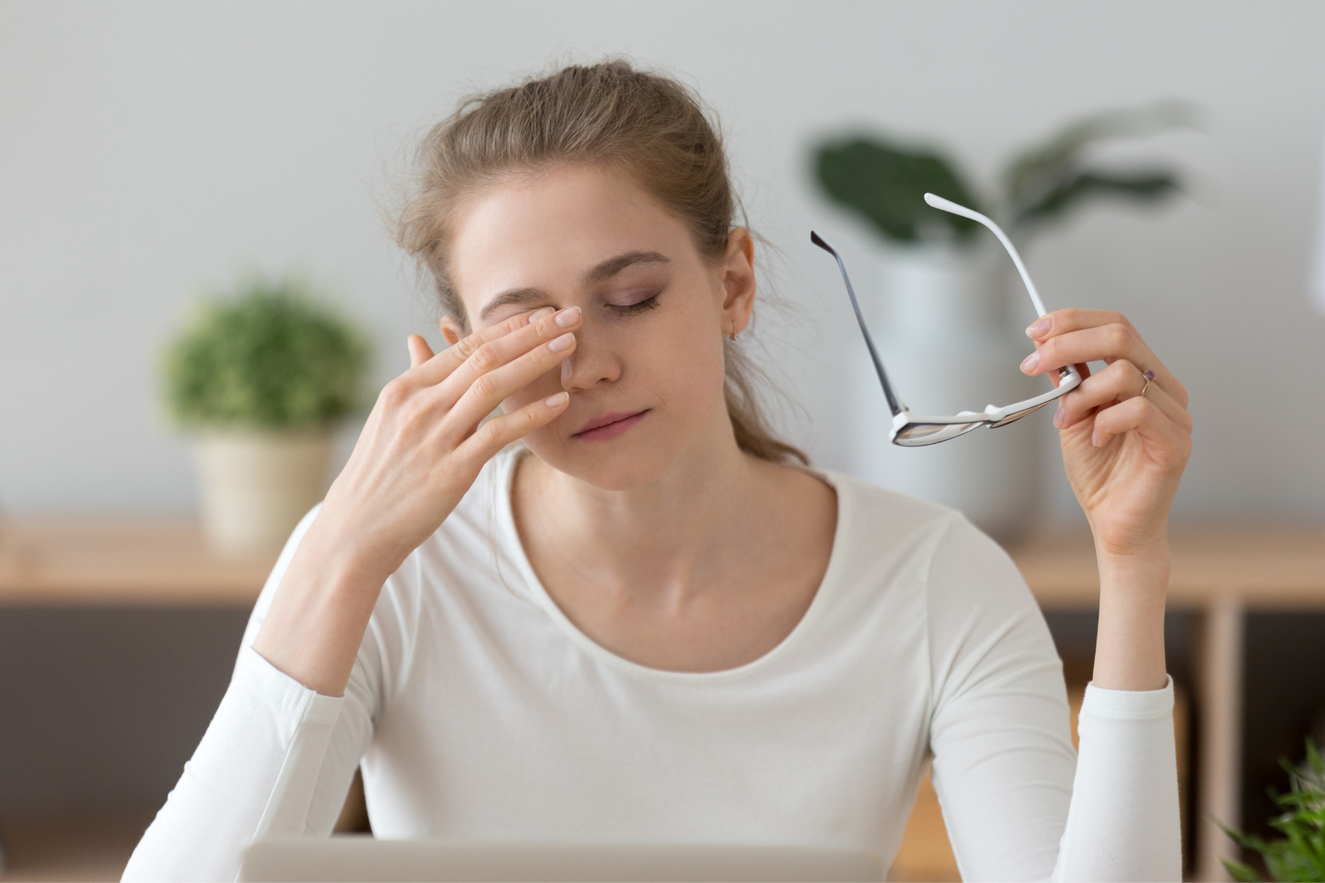 Woman rubbing her eyes while holding eyeglasses, appearing tired or strained