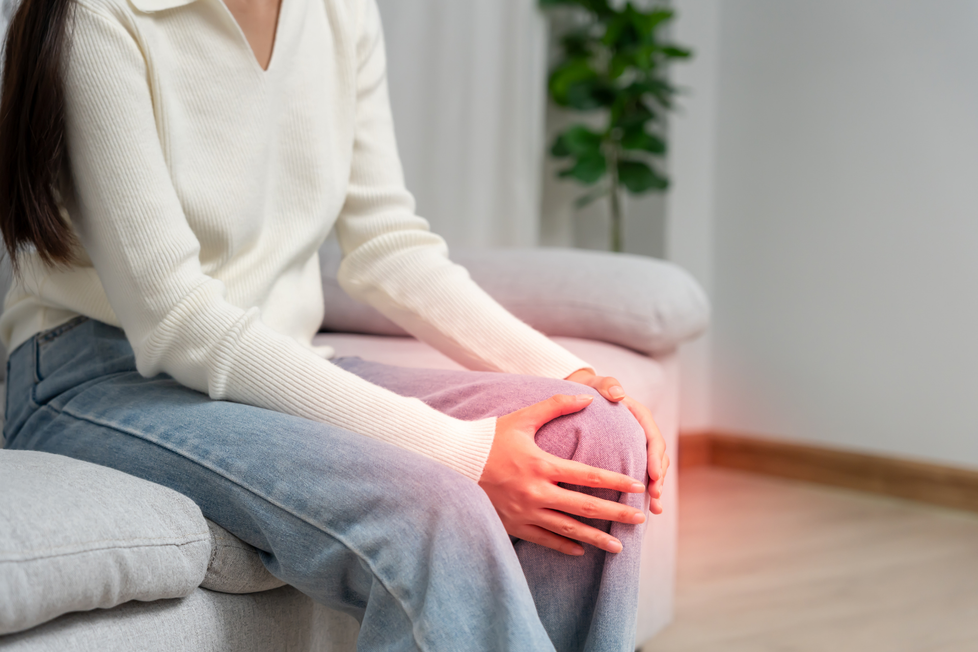 Woman sitting on a couch holding her knee with highlighted pain area