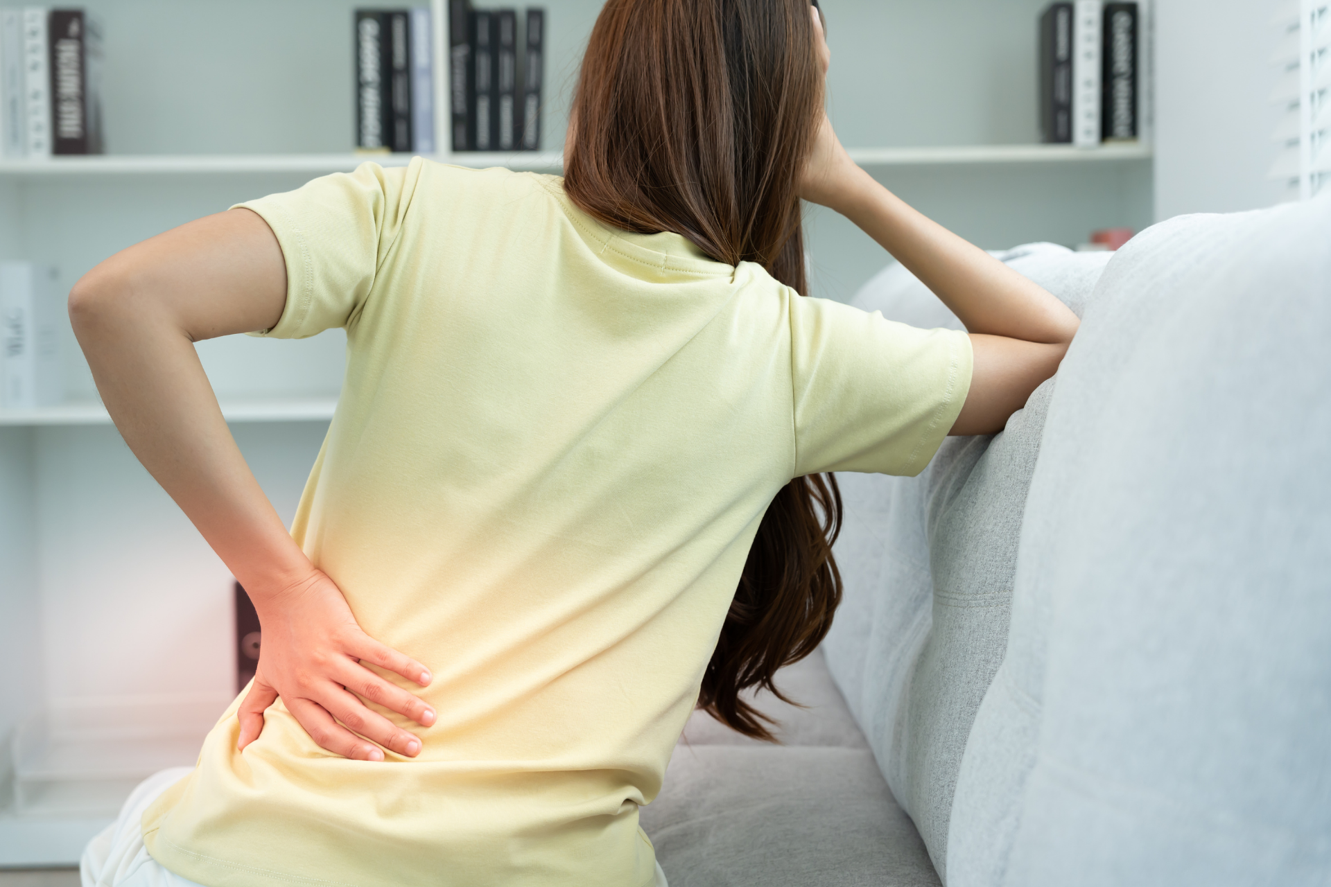 Woman sitting on a couch holding her lower back in pain