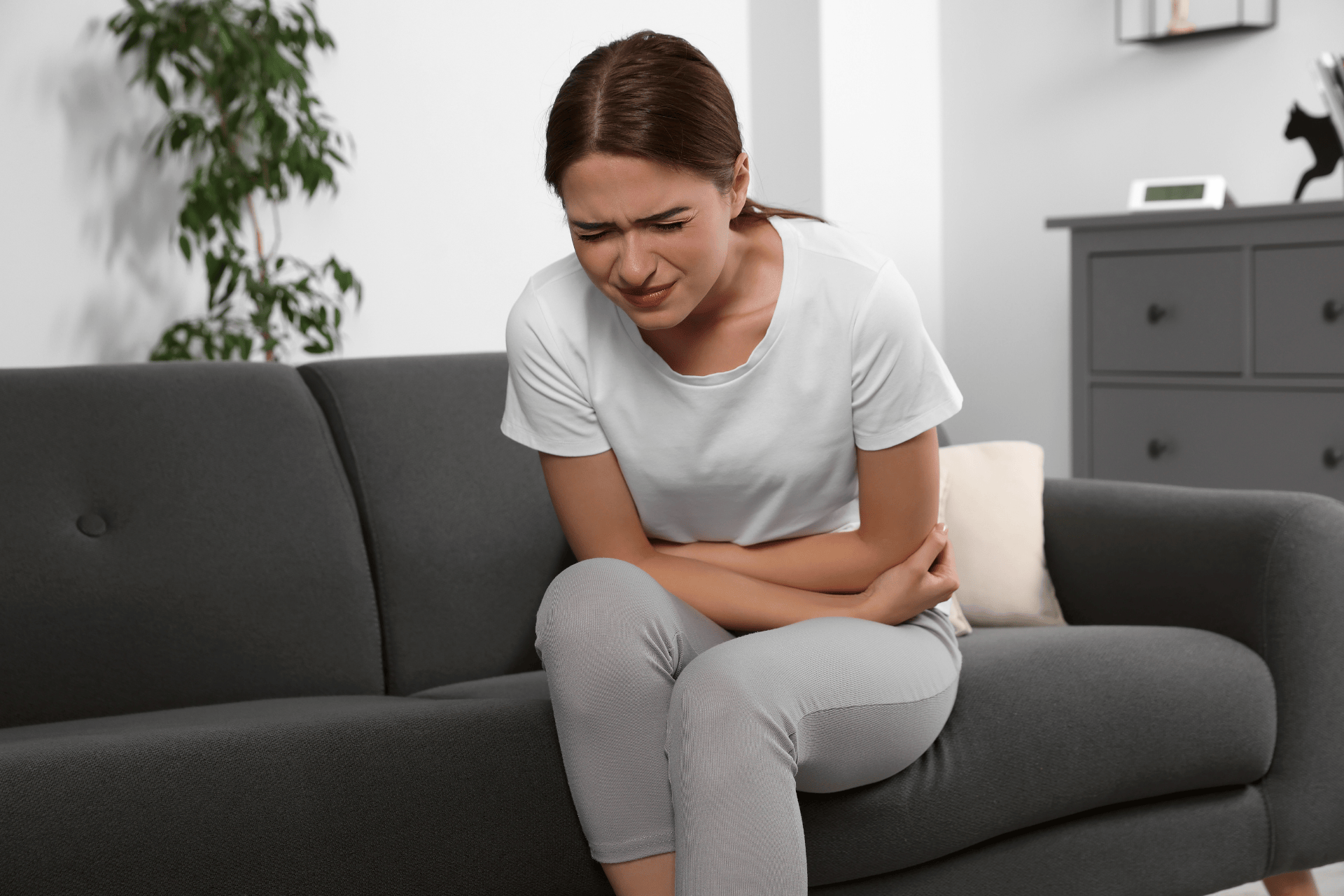 Woman sitting on a couch holding her stomach in pain, showing symptoms of a urinary tract infection (UTI).