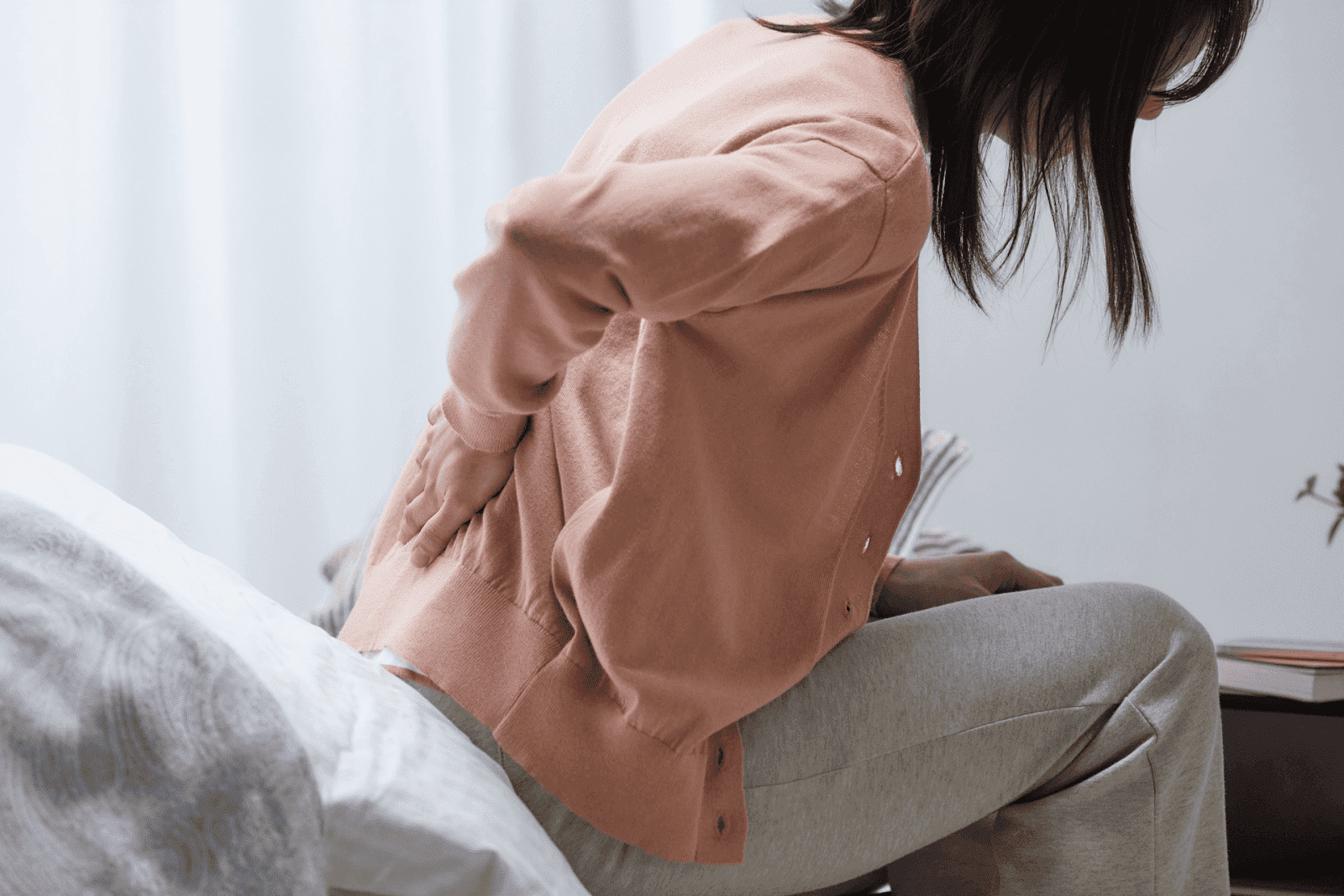 Woman sitting on bed holding her back in pain