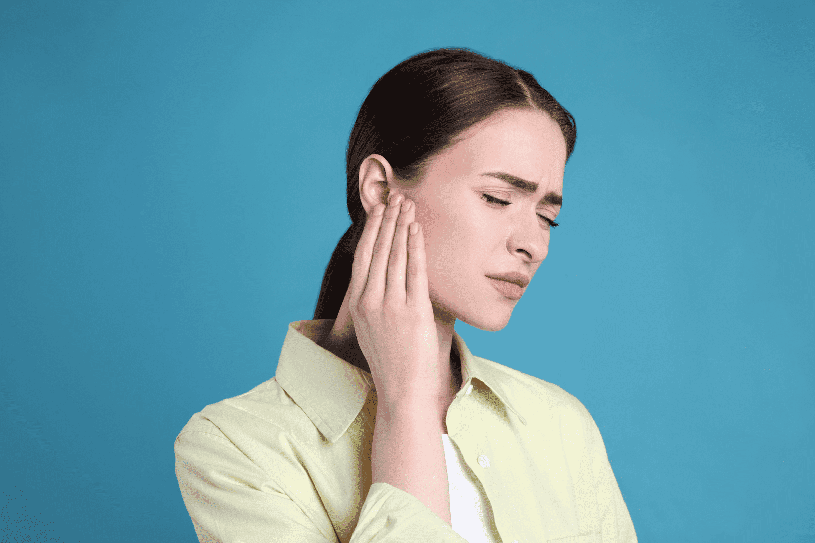 Woman touching her ear with a painful expression.