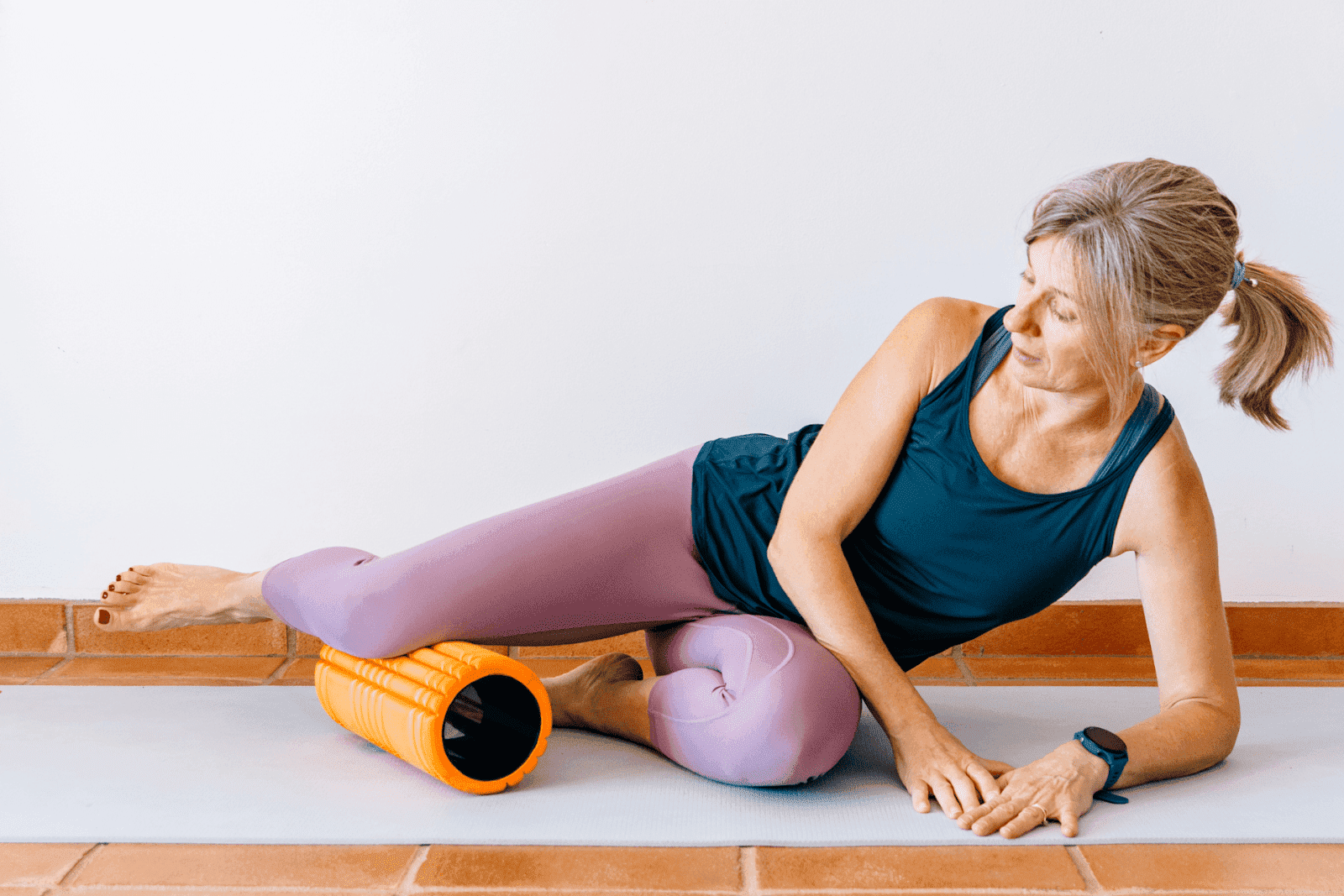 Woman using an orange foam roller on her thigh.