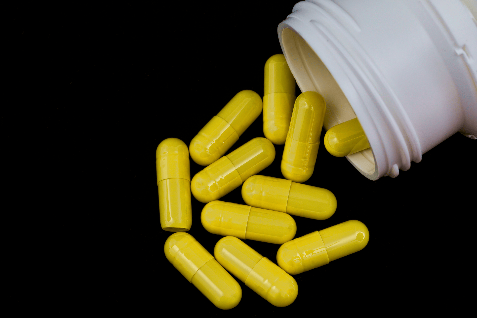 Yellow capsules spilled from a white medicine bottle on a black background