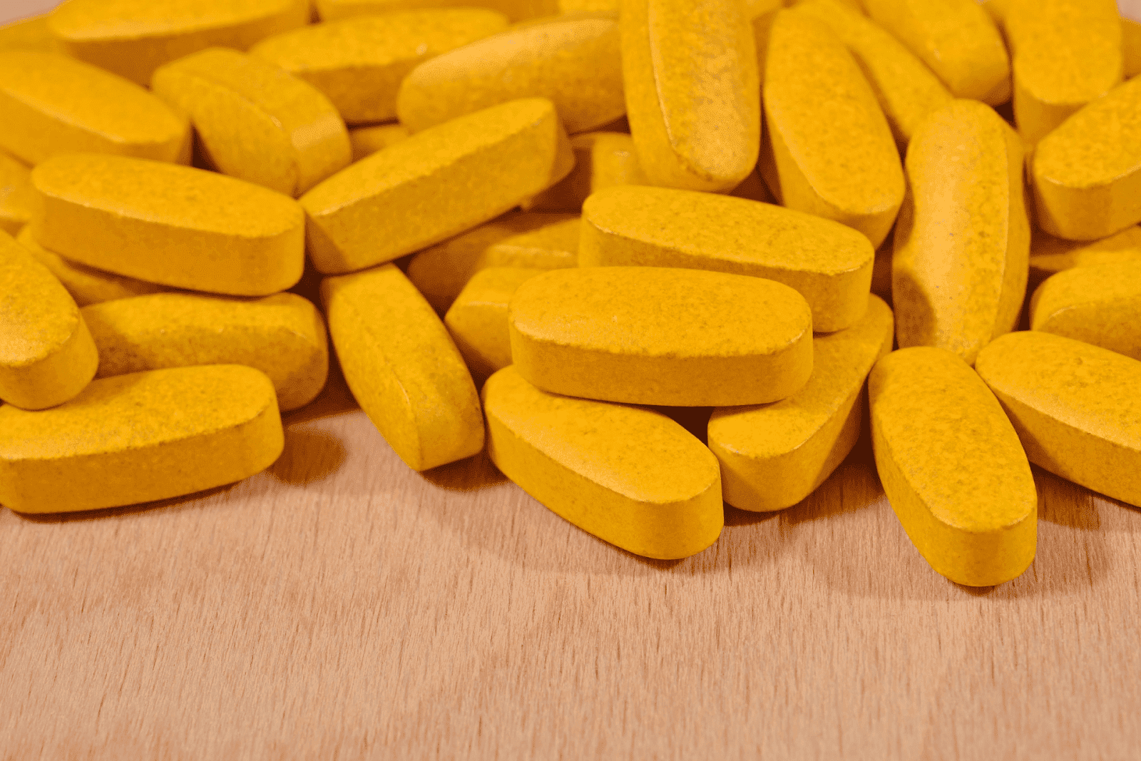Yellow oblong tablets spread out on a wooden surface.