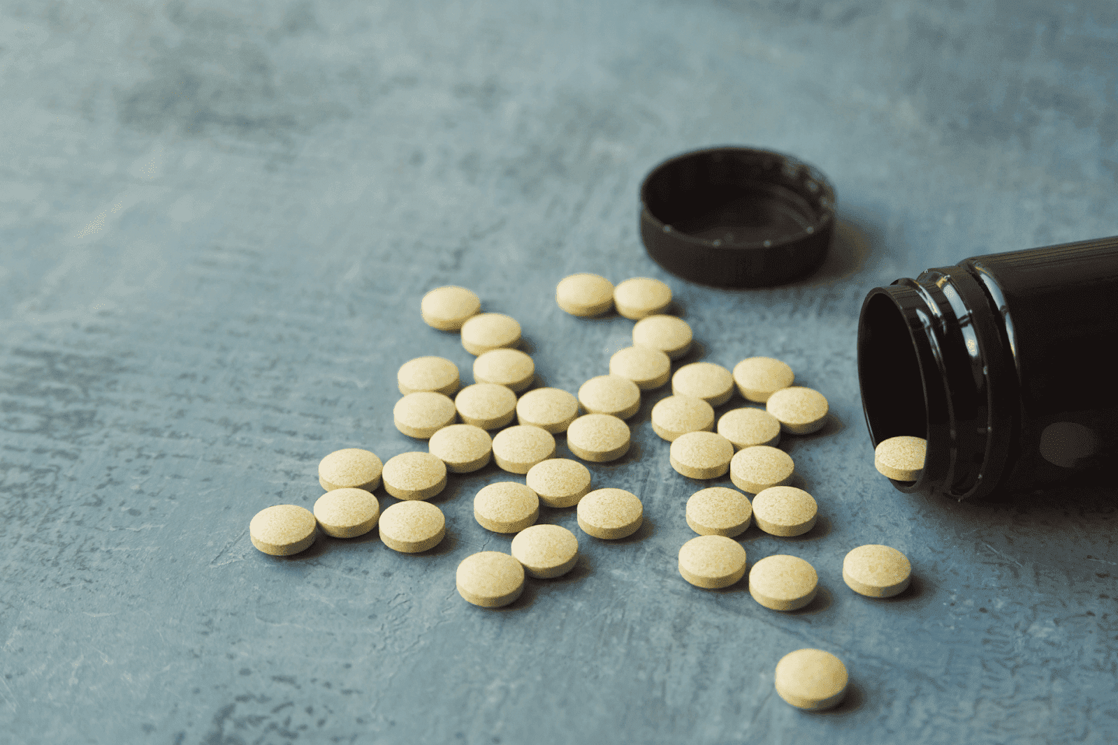 Yellow tablets spilled from an open brown bottle onto a gray surface.