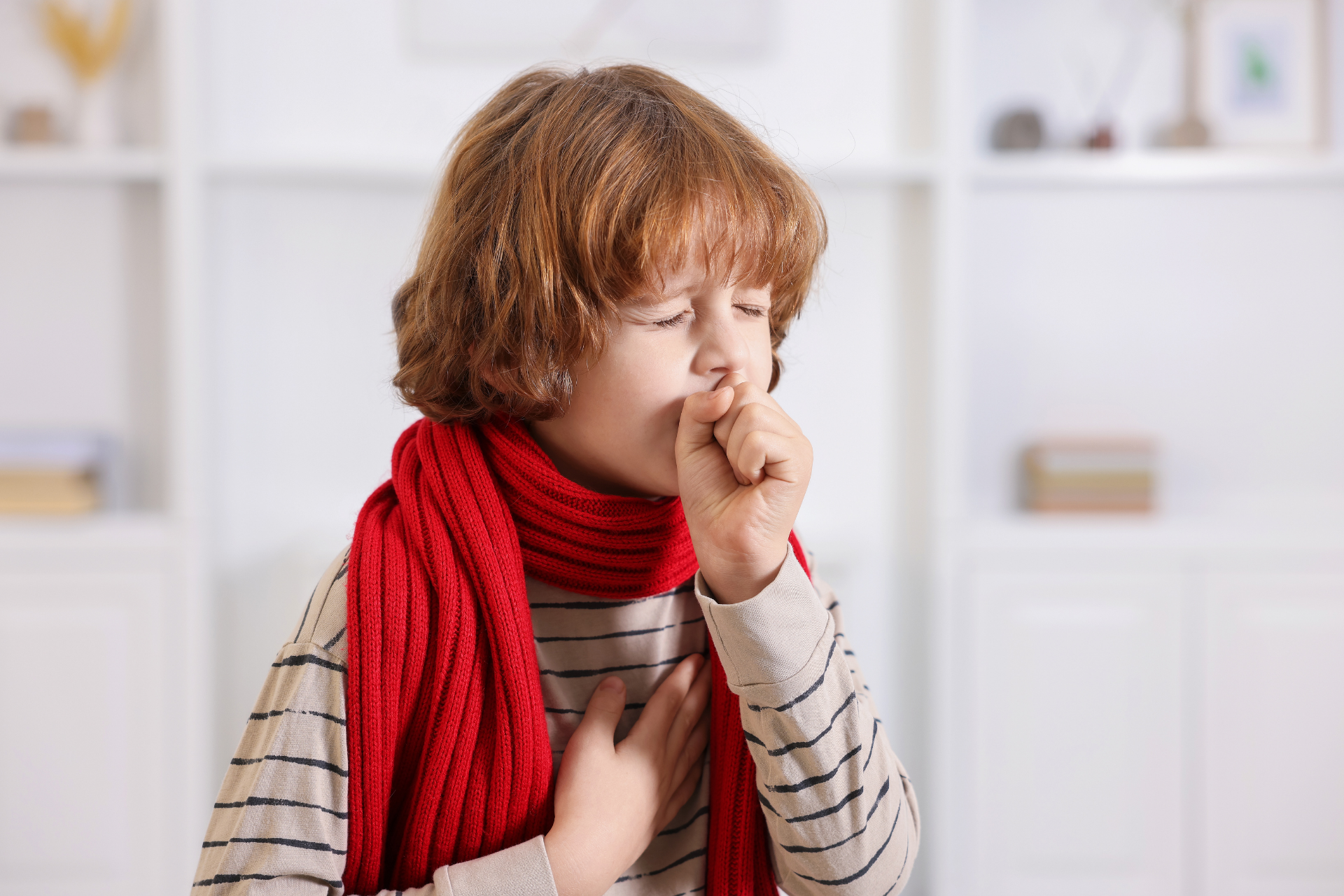 Young child wearing a red scarf, coughing into their hand indoors