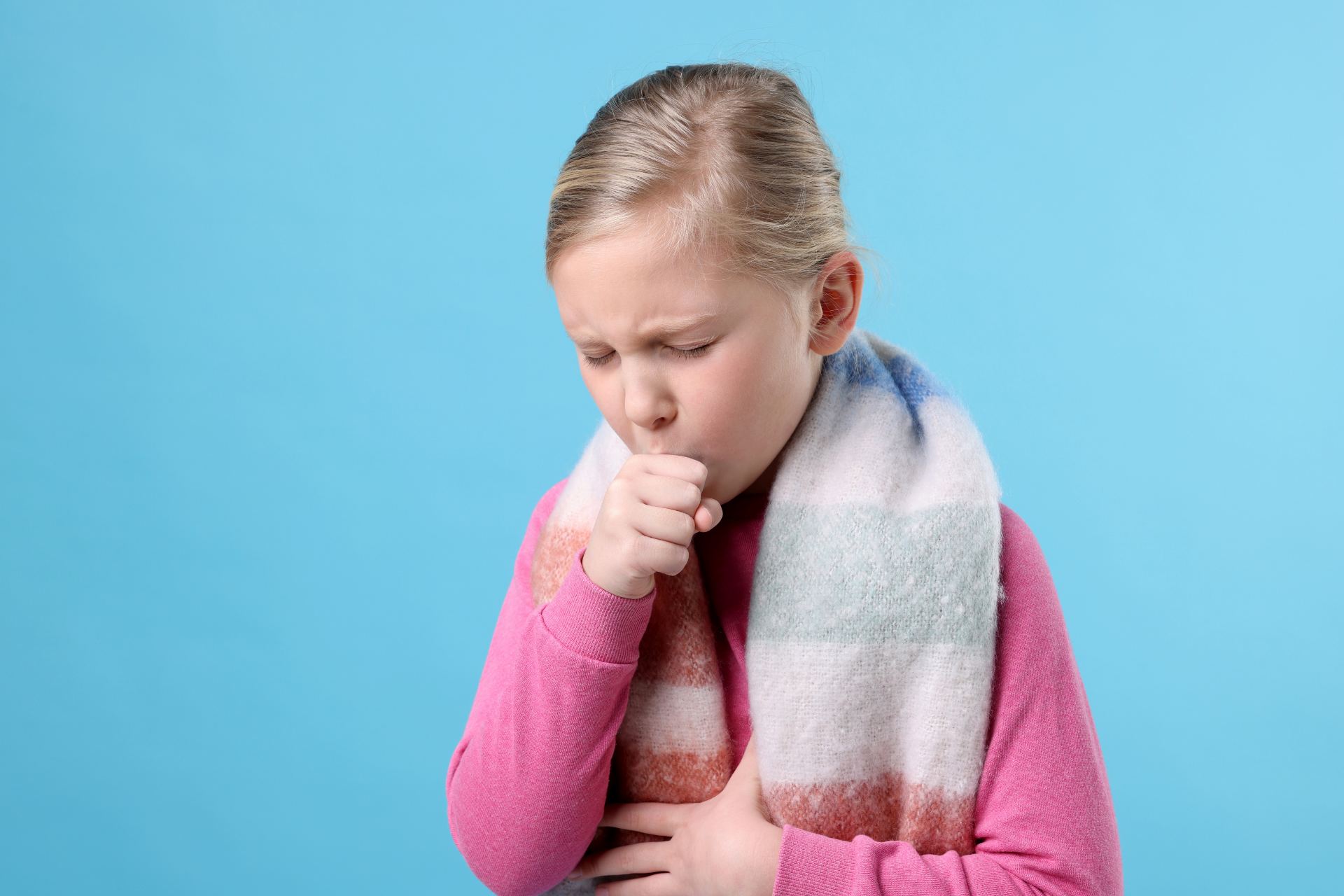Young child wearing a scarf, coughing into their hand against a blue background