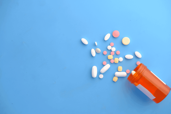 An orange pill bottle tipped over with various colorful pills and tablets scattered on a blue surface