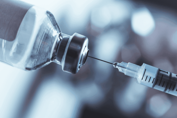 Close-up of a syringe needle inserted into a medicine vial, preparing to draw liquid for injection