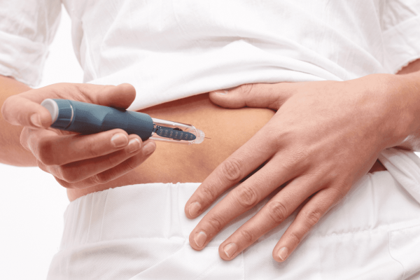 Person administering an insulin injection into their abdomen using a blue insulin pen