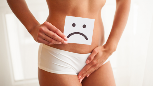 Woman with one hand on lower abdomen and another holding a paper with a sad face.