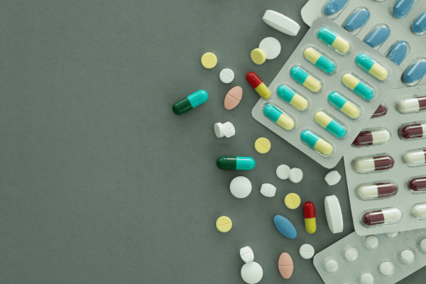 Various colorful pills and capsules scattered beside blister packs on a gray surface.