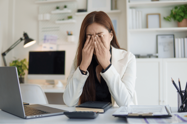 Stressed woman sitting at a desk with her hands covering her face.