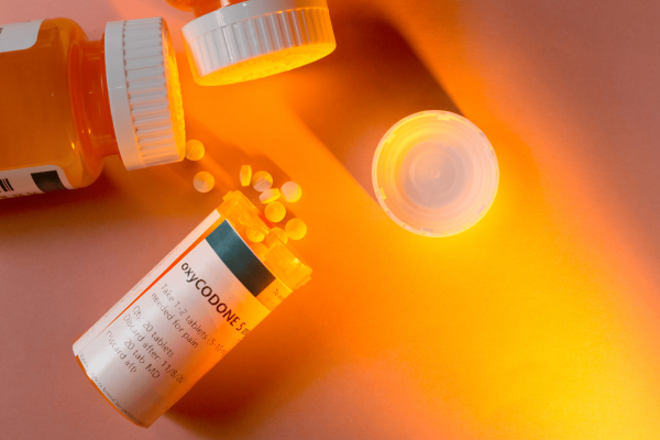 Prescription bottle labeled Oxycodone with spilled white pills under warm light