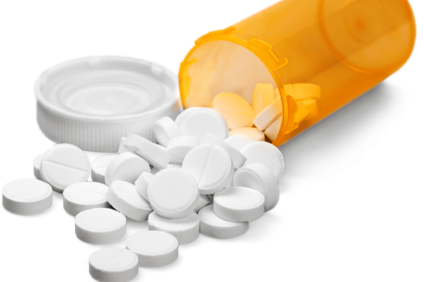 White tablets spilling out of an orange prescription bottle with the lid beside it.