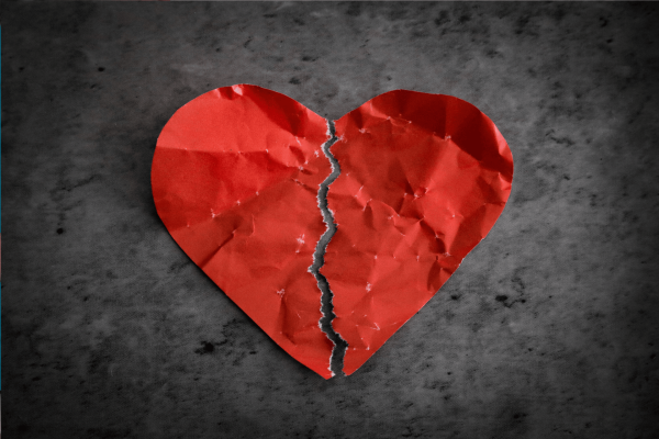 Crumpled red paper heart torn down the middle on a dark surface.
