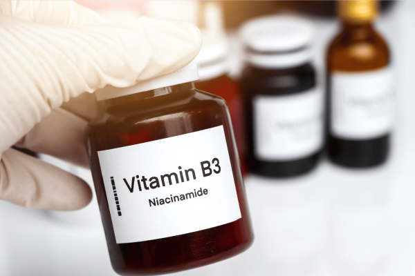 Gloved hand holding a bottle labeled Vitamin B3 Niacinamide.